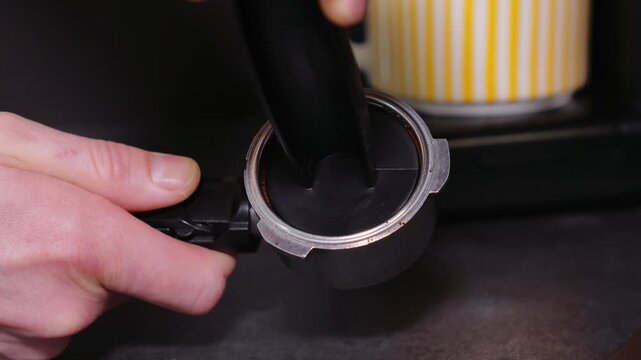 Close-up of a barista tempering freshly ground coffee with a tempera in a coffee shop. The process of making espresso. Footage of barista tamping coffee in pitcher of a barista crafting an Americano. 