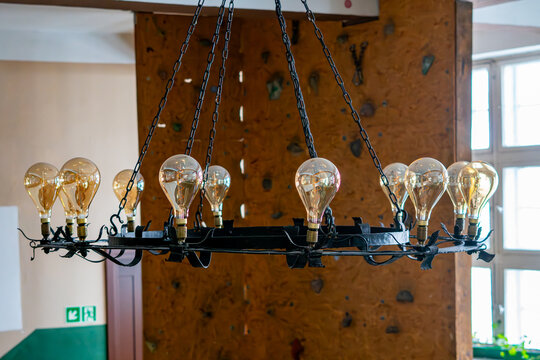 Large rustic wrought iron chandelier with Edison light bulbs, black metal construction hanging on chains, vintage lighting, interior of a tavern, hotel or restaurant, wooden wall background, retro atm