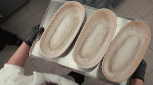 Baker in white uniform transfers shaped dough from proofing baskets to a tray, showcasing the process of preparing bread in a commercial kitchen setting