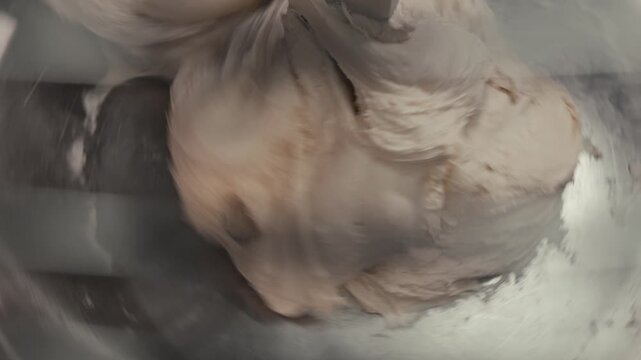 Mixing dough in a stainless steel bowl, showing the continuous blending of ingredients with a smooth, creamy texture and visible motion in the mixing process