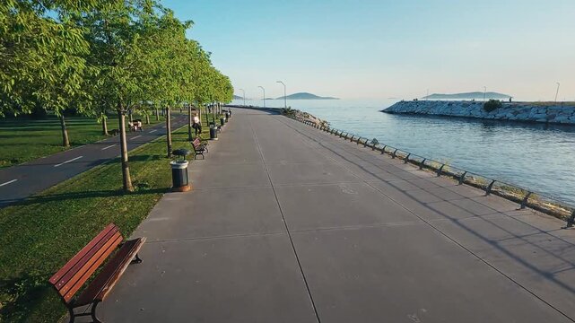 Smooth forward dolly shot along a seaside promenade with benches, trees and bike path beside calm Marmara Sea, Prince Islands visible on the horizon, Maltepe, Istanbul
