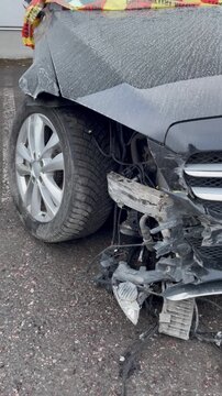 Vertical video of a severely damaged car after a traffic accident showing consequences of reckless driving and road safety violation with exposed wires broken bumper and twisted wheel