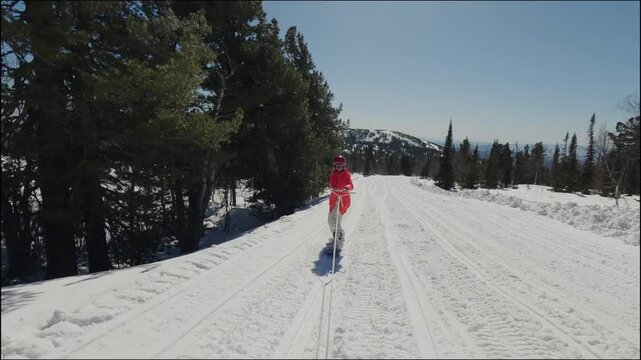 A snowboarder rides a snowmobile on a snowboard. A girl in ski clothes holds on to a rope and follows the vehicle. Snowboarding in the mountains on white snow.