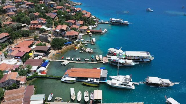 Aerial view of &Uuml;&ccedil;ağız waterfront village with tour boats and small craft moored at floating piers beside turquoise Mediterranean waters, Kekova, Antalya, Turkey