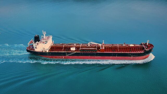 Large oil tanker underway on open blue sea, aerial side view showing full hull length with bow wave and wake, global trade concept