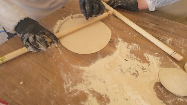 Close-up of traditional Turkish flatbread dough being rolled with wooden rolling pin, handmade pastry preparation
