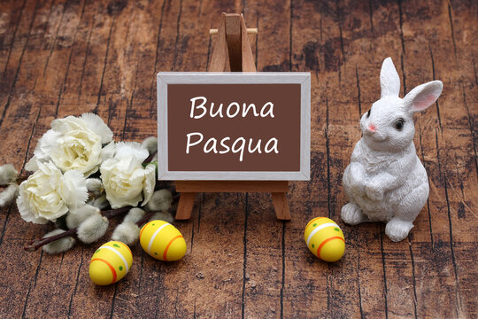 Decorazione pasquale con coniglietto bianco, uova e una lavagna con la scritta italiana "Buona Pasqua" su sfondo di legno.