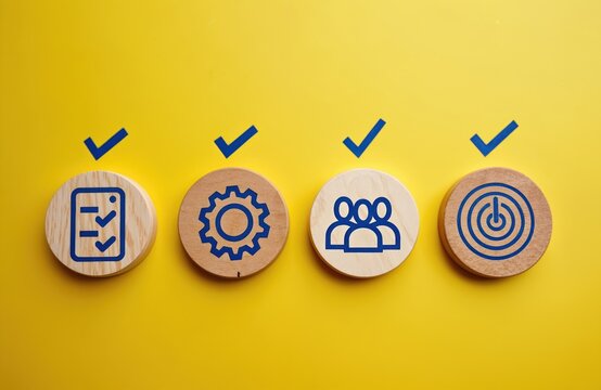 Four wooden circles with icons of checklist, gear, people, and target are placed on yellow background. Each icon has a blue checkmark above it. Concepts include strategy, process, team, goals.