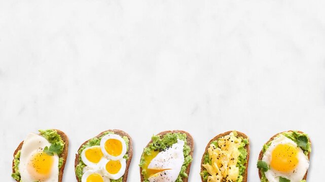 Variety of avocado egg toasts on sourdough bread. Moving bottom border. Stop motion loop video on a white marble background. Fried, boiled, poached and scrambled.