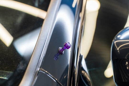 Violet plastic sticker with glue to make dent removal procedure at car after hail. Process of paintless dent repair on car body. The mechanic at the auto shop with tools to repair dents in car body. 