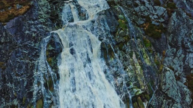  Aerial mid-range shot of a beautiful waterfall in Wicklow, Ireland, surrounded by vibrant green vegetation and rocky terrain.
