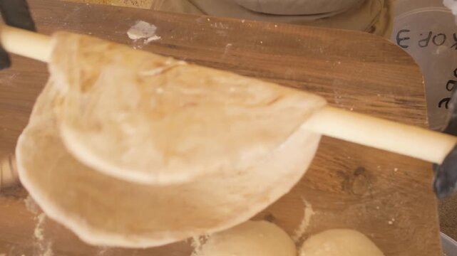 Close-up of traditional Turkish flatbread dough being rolled with wooden rolling pin, handmade pastry preparation