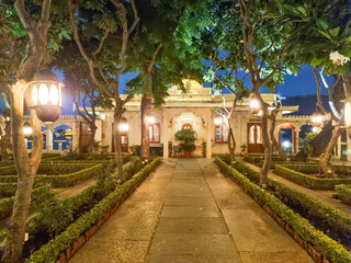 Obraz premium Beautiful night view of Jagmandir Island Palace in Udaipur with glowing lights, symmetrical garden pathway, trees, and heritage architecture reflecting royal ambiance in India
