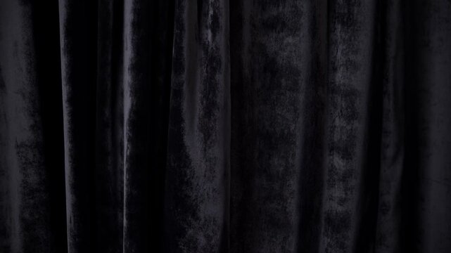 Slow pan of black velvet curtains gently swaying on stage backdrop in dim theater studio interior revealing textured drapery and shadowy folds
