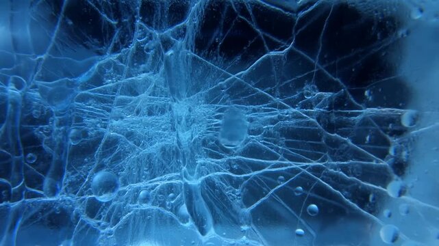 Slow motion dolly in on frozen water bubbles and ice cracks inside translucent blue ice block in studio
