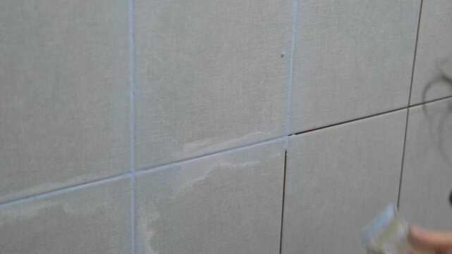 Worker using a rubber grout float to smooth grout between tiles. Carefully applying sealant to tiles joints. Workman hands smoothing caulk, using small tool to remove excess and create clean seam.