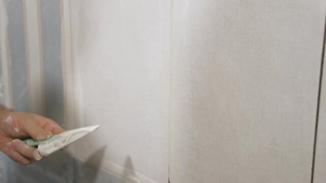 Worker using a rubber grout float to smooth grout between tiles. Carefully applying sealant to tiles joints. Workman hands smoothing caulk, using small tool to remove excess and create clean seam.