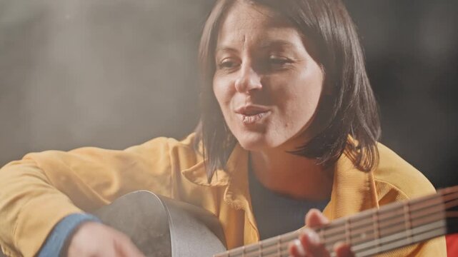 Lady sings softly beneath starry night sky. Female vocalist with gentle voice beside glowing campfire. Woman with reflective mood singing softly near flickering firelight under starry sky