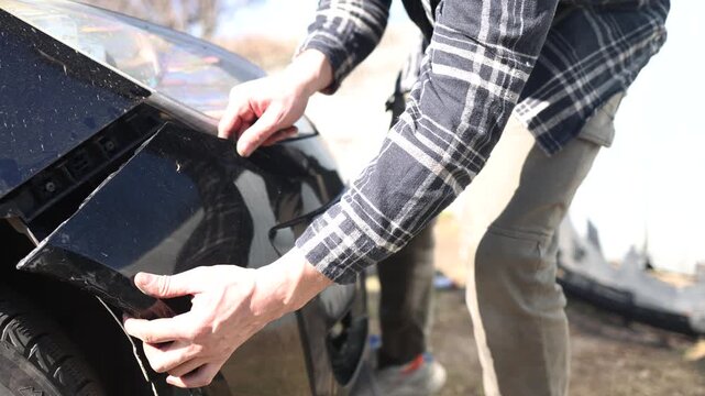 close up of the mechanic's hands, who removes the bumper of the car, he repairs the car.