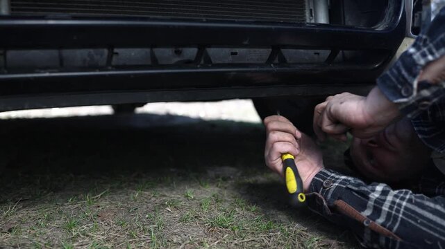 close up of the mechanic's hands, who removes the bumper of the car, he repairs the car.
