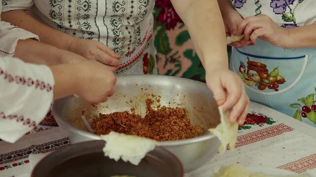 Group of women in traditional clothing prepare stuffed cabbage rolls, filling cabbage leaves with a savory mixture in a rustic kitchen setting with colorful textiles
