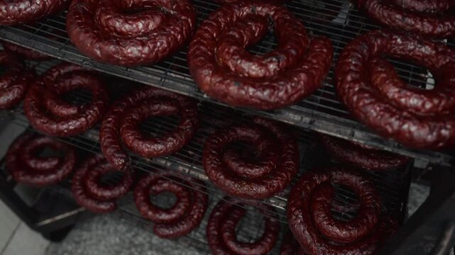Dark brown circular sausages arranged in spiral shapes on metal racks, showcasing the drying process in a food preparation area with visible textures and details
