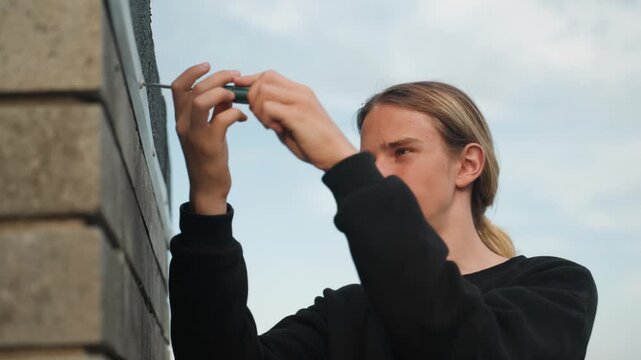 Person securing hook carefully. Skilled handyman securing metal hook against cloudy sky background. Casual installer methodically tying string to metal hook under overcast sky conditions