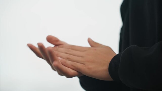 Overcast hands warming with brisk rubs, person in black sweater vigorously rubbing palms and interlacing fingers, outdoor cool light, knuckle motion and squeeze suggest cold hands or preperformance