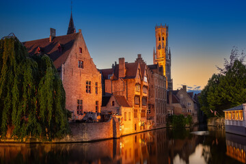 Fototapeta premium Canal view of Rozenhoedkaai and the Belfry of Bruges at dusk in Belgium. Historic medieval architecture reflects in the Dijver canal water under a twilight sky in the Flanders region.