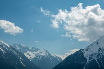 Naklejka premium Bright sky with clouds over tall snowy mountains