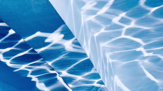 The abstract reflection of rippled water creates dynamic patterns of light on the concrete wall, capturing movement, texture, and the interplay of natural light.