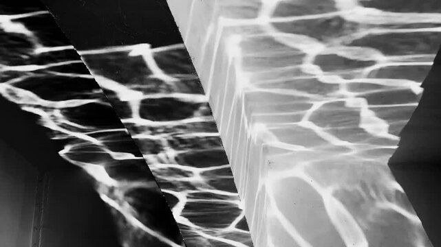 The abstract reflection of rippled water creates dynamic patterns of light on the concrete wall, capturing movement, texture, and the interplay of natural light.