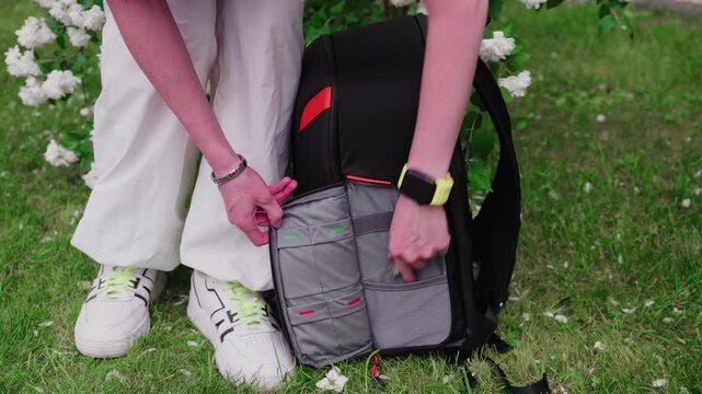 A woman's hands open a backpack for a photo. Close-up of the photo backpack. The girl takes the keys out of her backpack pocket.