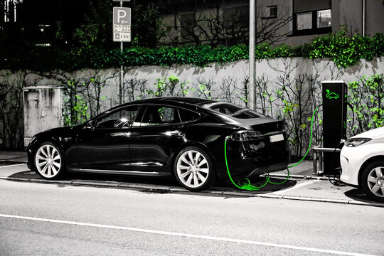 Tesla Electric Car Charging at Public Station &ndash; EV Infrastructure, Sustainable Mobility and Urban Night Scene. Electric car charging,  featuring highlighted green cable and green wall vegetation.