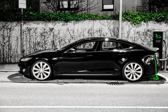 Tesla Electric Car Charging at Public Station &ndash; EV Infrastructure, Sustainable Mobility and Urban Night Scene. Electric car charging,  featuring highlighted green cable and green wall vegetation.