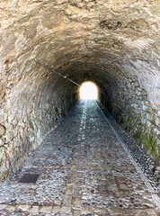 Fototapeta premium Stone tunnel and cobblestone path inside Corfu island New Fortress, Greece. Bright day light at the exit