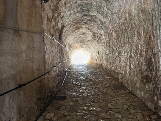Fototapeta premium Stone tunnel and cobblestone path inside Corfu island New Fortress, Greece. Bright day light at the exit