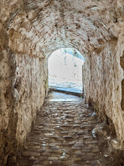 Fototapeta premium Stone tunnel passage inside the Old Fortress in Corfu Old Town, Greece. A bright exit over cobblestone path