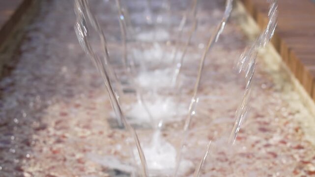 Clear water streams fall into a textured basin. Each stream glints, creating a soothing visual rhythm. Water splashes gently, producing fine mist and bubbles