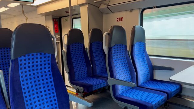 Modern blue passenger seats inside a regional train carriage in Germany. Empty interior of a clean public transport train with window view.