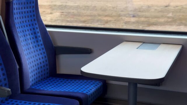Interior of a modern regional train with blue patterned seats and a white table by the window. Comfortable passenger area in a European train.