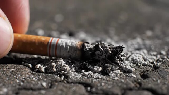 Close up of a burning cigarette butt with ash on a dark textured surface