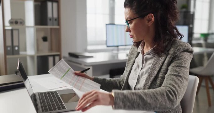 Woman analyst accountant reviews finance paperwork on laptop. In a bright office she checks reports, balances budgets and updates data daily. Concept of accurate financial record management.