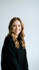 Obraz premium Young Caucasian businesswoman with blonde wavy hair smiling confidently in black sweater against white background for professional headshots.