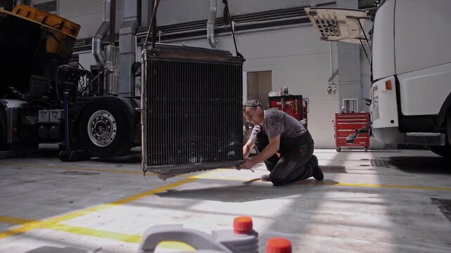Professional auto locksmith repairs a large radiator from a truck engine in a company facility 