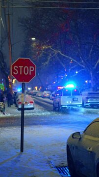 Snowy city street at night with stop sign and police. Winter street scene in New York featuring a stop sign in focus and a police vehicle with blue lights.