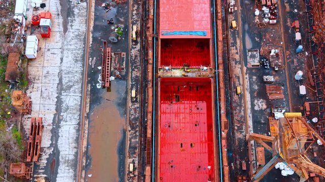 Top down view of empty red cargo ship hold at shipyard. Aerial close up of open red painted cargo holds of a vessel docked for maintenance or loading.