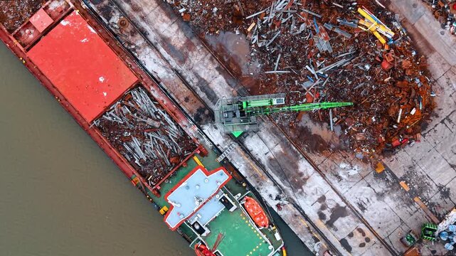 Close up aerial view of crane loading scrap metal. Detailed top down shot of green hydraulic grab crane loading recycled steel into ship hold.