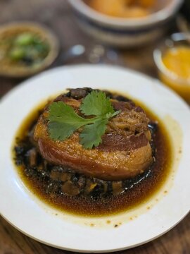 Traditional Chinese braised pork belly Khao Yok served on white plate with dark soy sauce and fresh cilantro garnish