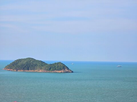 Rat Island rising from calm turquoise Gulf of Thailand with cargo ships on distant horizon, Songkhla, Thailand